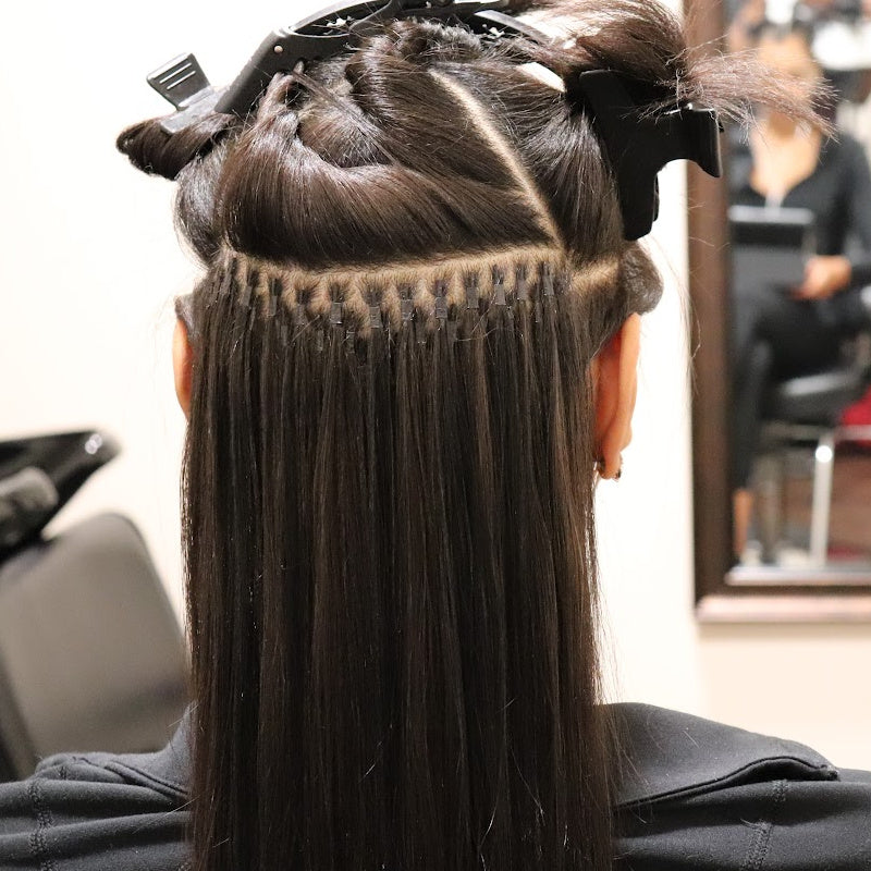 Close-up of microlink hair extension installation on straight hair, showing strand-by-strand attachment for a flawless blend.
