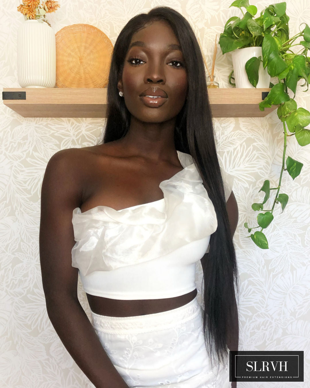 Woman wearing a white one-shoulder dress with a black belt, standing against a neutral background with decorative elements.