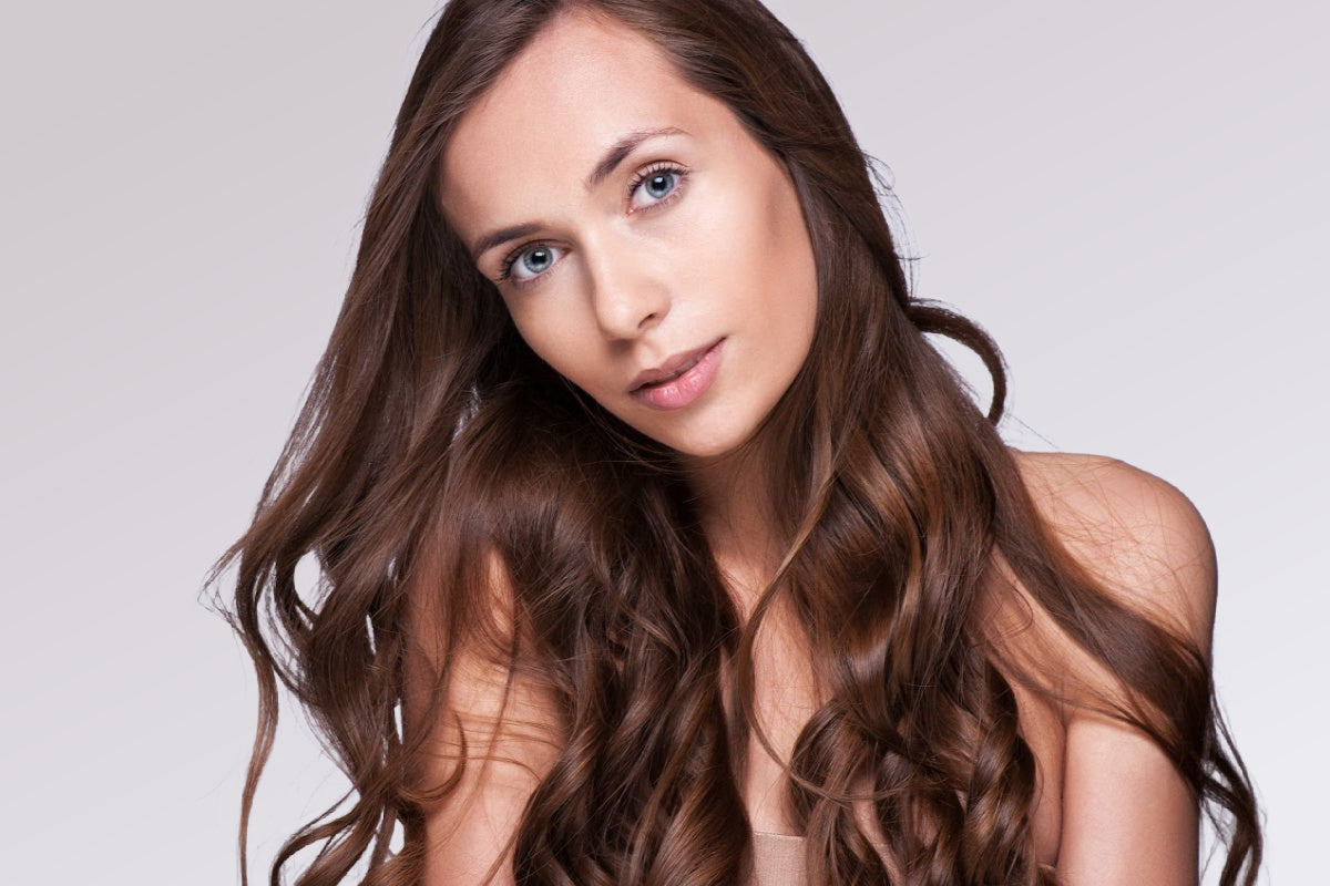 Woman with long, wavy brown hair against a plain background - SL raw Virgin Hair