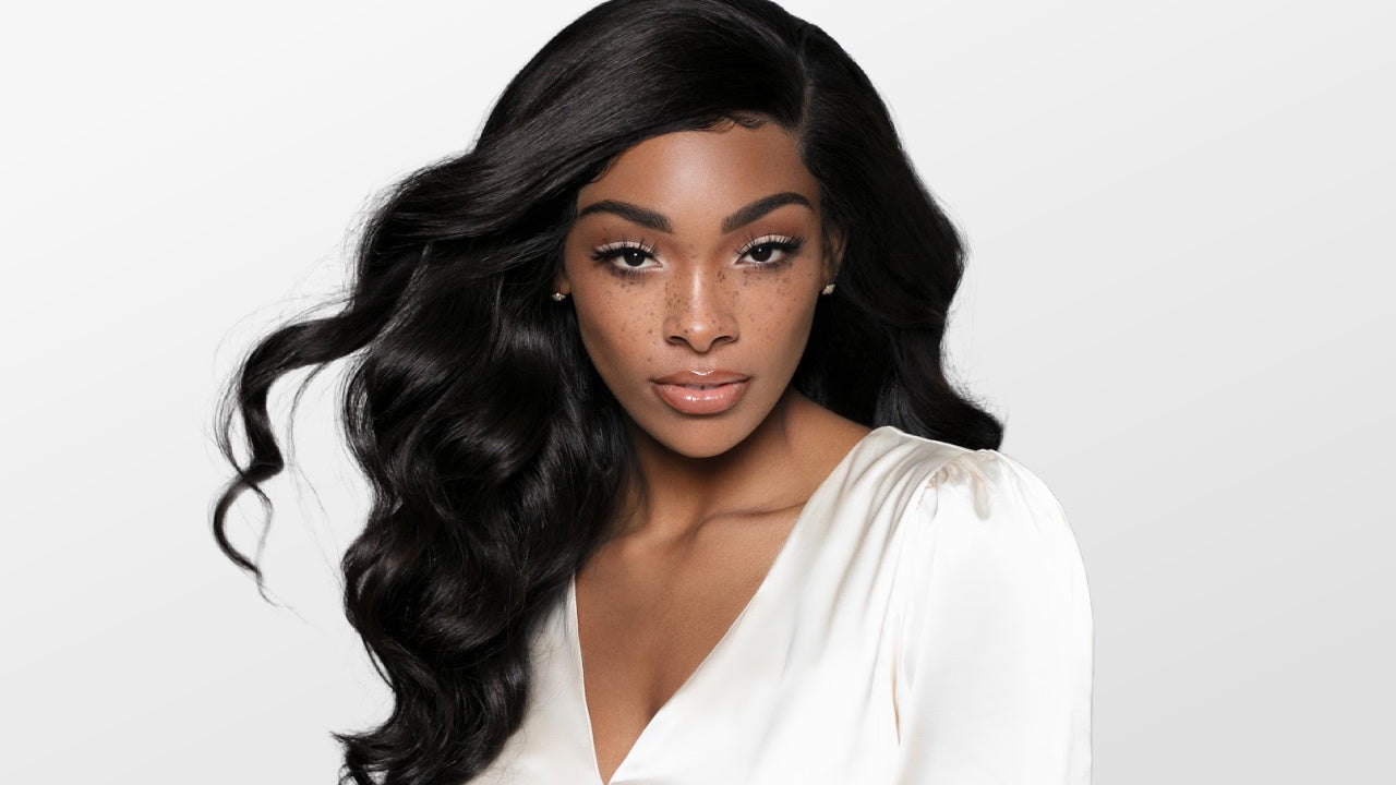 Woman with long, wavy black hair wearing a white top on a light gray background by SL Raw Virgin Hair