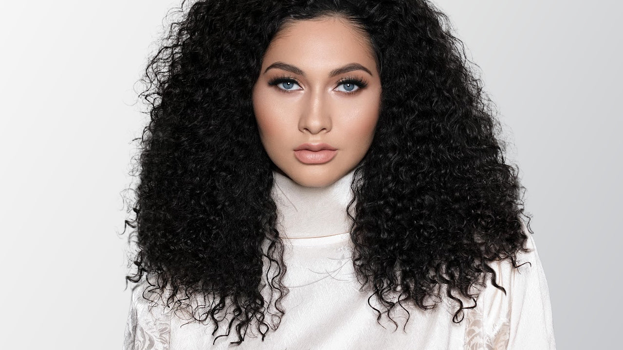 Woman with long, curly black hair wearing a white outfit against a light gray background