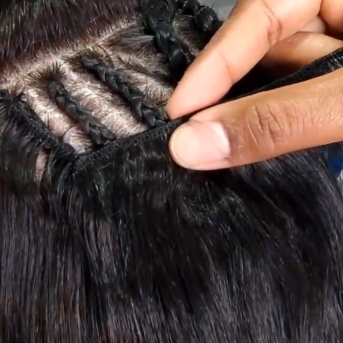 Close-up of a  hair extension weft being applied to a person's hair, showing the braided attachment and individual strands.