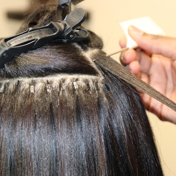 A person getting hair extensions applied with beads.