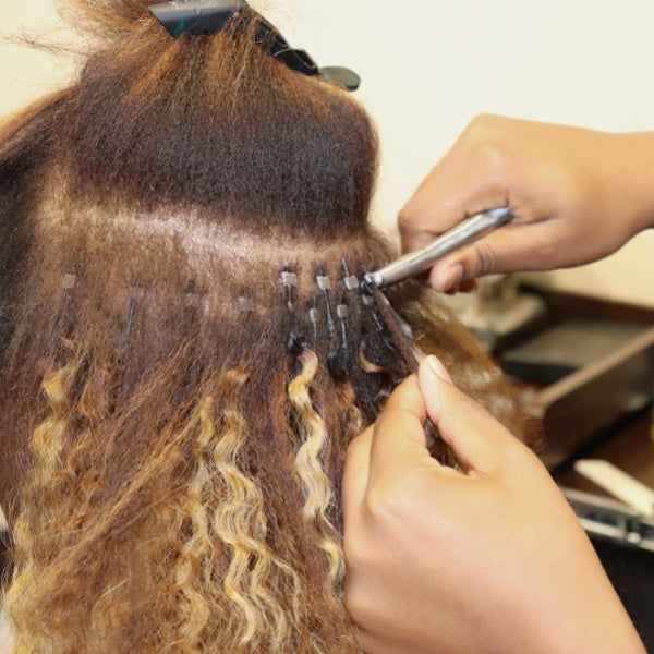 A person is clamping a microbead on a hair extension with a tool