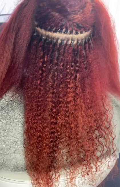 Cliente portant des extensions I-Tip Soft Kinky Curly de SL Raw Virgin Hair, de couleur rouge.