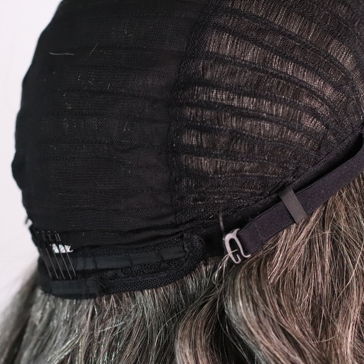 Close-up of natural gray wig cap showing adjustable strap, rear comb and ventilated construction