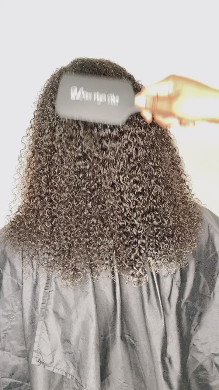 Hand using SL Raw Virgin Hair® detangling brush on kinky curly human hair extensions to demonstrate gentle maintenance and texture definition.